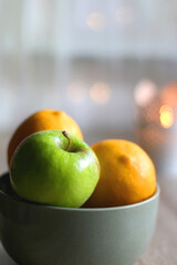 Bowl of lemons and apples, candle holder with lit candle and vase with gypsophila flowers on the table. Bokeh lights in the background. Selective focus.