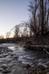 Winter river with flowing water little  village and trees in the background sunset light long exposure silky water effect 