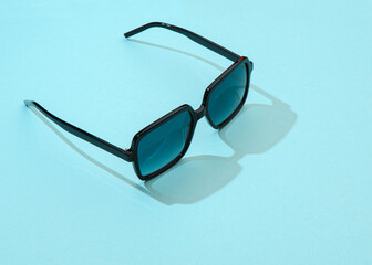 Women summer sunglasses on pastel blue background in sunlight. Modern stylish sunglasses for...