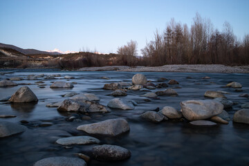 River with rocks and mountains in the background blue sky and some trees in winter long exposure