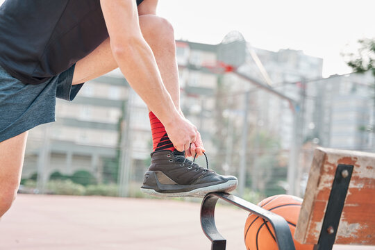 unrecognisable basketball player tying shoelaces on a court