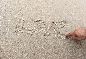 Young man hand writing word love in cursive on sand beach Beach love concept.