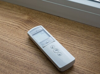 White remote control panel for motorized roller shades or automatic blinds lies on a wooden...