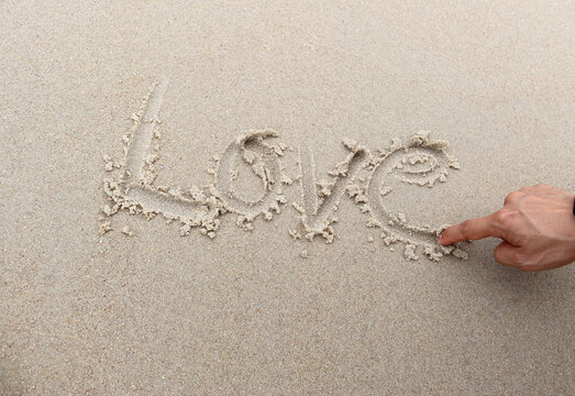 Young man hand writing word love in cursive on sand beach Beach love concept.