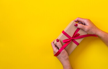 Woman hands holding gift, yellow background.