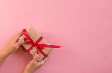 Woman hands holding gift with red ribbon on pink background, copy space. Flat lay, hands and present box, top view. Valentine or love, spring holidays, Christmas and birthday concept.