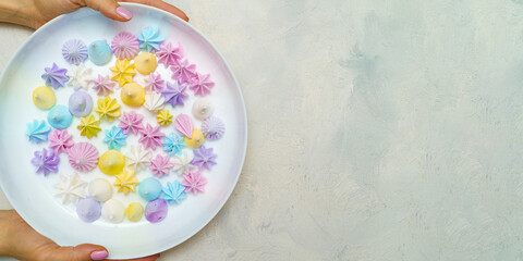 Top view of hands wich holds plate with delicious colorful meringue cookies . Sweet decor. Easter