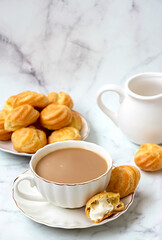 Karak chai or Masala tea and homemade profiteroles stuffed with whipped cream. On marble light background.