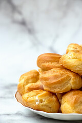 Homemade profiteroles stuffed with whipped cream On marble light background.