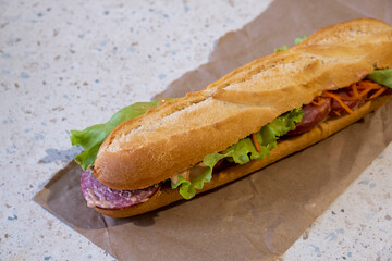 Large baguette sandwich with salami, lettuce, cheese and sauce. Selective focus. Close Up.