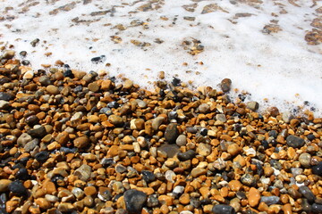 Wet stones from a pebble beach with sea foam - natural texture or background or wallpaper