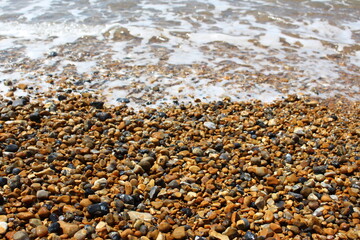 Wet stones from a pebble beach with sea foam - natural texture or background or wallpaper (Brighton Beach, England)