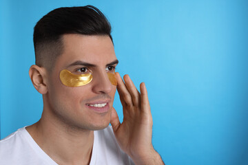 Man applying golden under eye patch on light blue background. Space for text