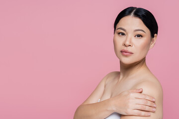 Asian woman with naked shoulders looking at camera isolated on pink