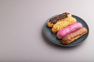Set of eclair, traditional french dessert on blue ceramic plate on gray pastel background. side view, copy space.