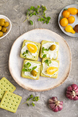 Green cracker sandwiches with cream cheese and tomatoes on gray concrete background. top view, close up.