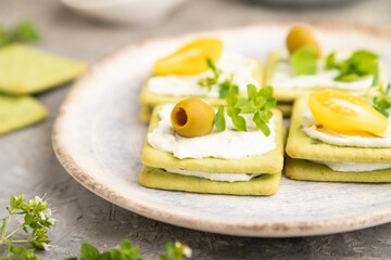 Green cracker sandwiches with cream cheese and tomatoes on gray concrete background. side view, close up.