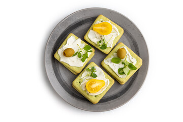 Green cracker sandwiches with cream cheese and tomatoes on gray plate isolated on white background. top view