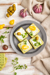 Green cracker sandwiches with cream cheese and cherry tomatoes on white wooden background. top view, close up.