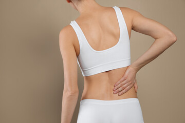 Woman suffering from pain in back on beige background, closeup