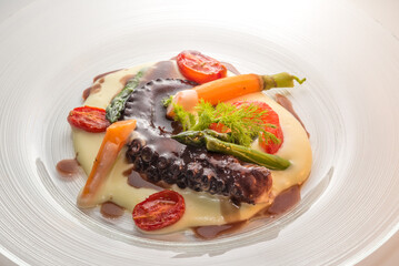 Octopus tentacle stewed in red wine on mashed potatoes with asparagus, carrot, fennel and tomato. Close up in glass plate