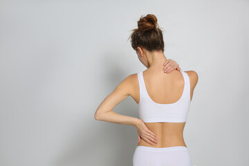Woman suffering from pain in back on light grey background. Space for text