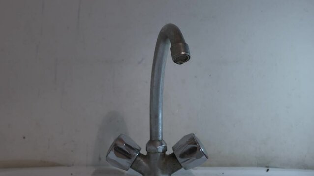 Drop of water flows from broken kitchen metal faucet. Household conception.