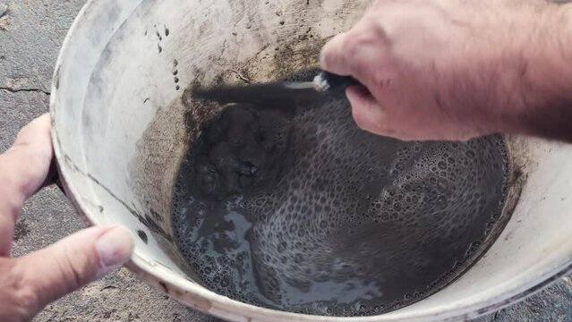 A construction worker hand mixing cement and water with spatula and making concrete in a white oval bucket. Point of view shot