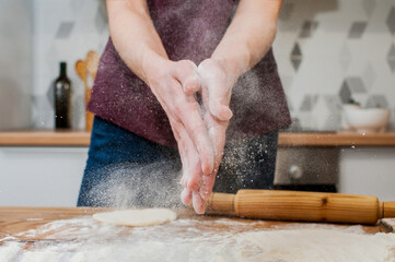 A woman in the kitchen prepares dough and claps her hands with flour, a splash of flour unfolds