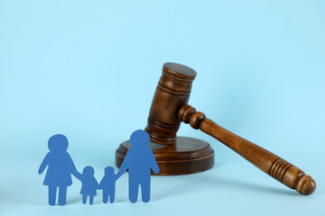 Paper family figure and wooden gavel on light blue background. Child adoption concept