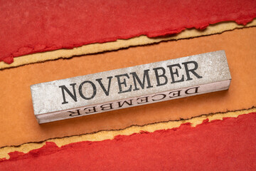 November text on grunge wooden block against handmade rag paper in red and orange tones, calendar concept