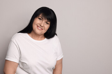 Fototapeta premium Beautiful overweight mature woman with charming smile on light grey background. Space for text