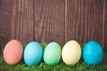 Colorful Easter eggs in the grass on wooden background.