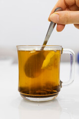 A glass cup of hot tea with honey and lemon on a light background.