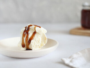 A scoop of ice cream topped with caramel. Behind is a jar of caramel