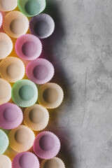 moldes de colores de papel para magdalenas alineados sobre un fondo gris claro con textura, con espacio en blanco