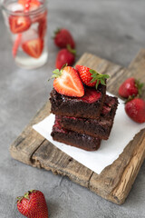 Pieces of fresh chocolate brownie with strawberries on a concrete background. Stack of fudgy chocolate brownies with strawberries on a concrete background. Homemade bakery and dessert.