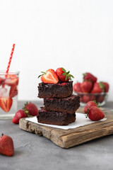 Pieces of fresh chocolate brownie with strawberries on a concrete background. Stack of fudgy...