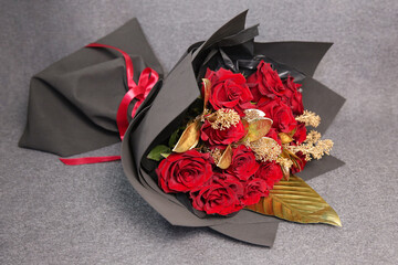 Bouquet of red roses with golden decorative branches in a black package