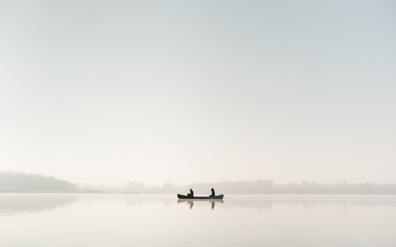 Silhouette of a canoe with two people on vast calm water surface