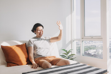 Asian man use his hand to cover the hot sunlight that shine on his living room. 