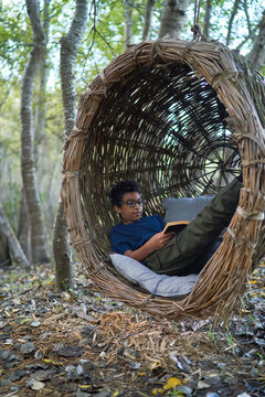 Boy reading book in nest swing in woods