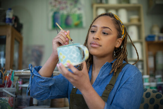 Young female artist painting ceramic mug in art studio