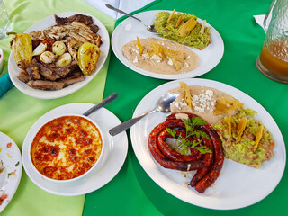Grilled various dishes with meat, melted cheese, guacamole, chorizo and beans