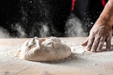 flying pizza dough with flour scattering in a freeze motion of a cloud of flour midair on black. Cook hands kneading dough. copy space