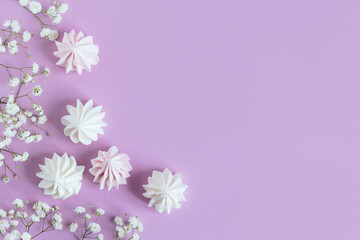 White marshmallows and flowers on a violet pastel background.