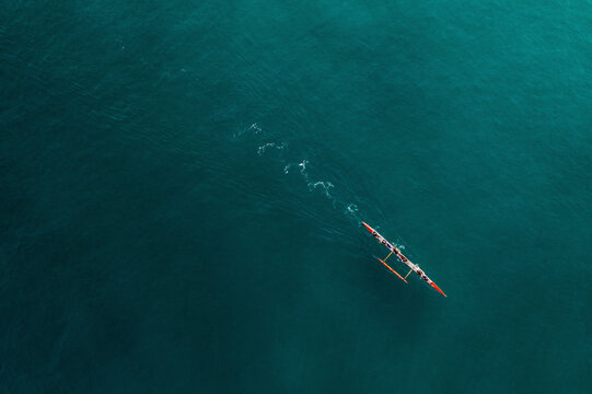 Aerial Top Down View Of People Paddling A Red Outrigger Canoe Across The Turquoise Ocean Water In Rio De Janeiro, Brazil.