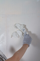 Putty the wall in the house with putty using a spatula to level the surface irregularities