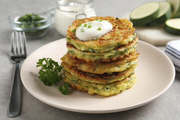 Delicious zucchini fritters with sour cream on grey table