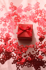 Small red giftbox and heart confetti on pale pink background. Selective focus.